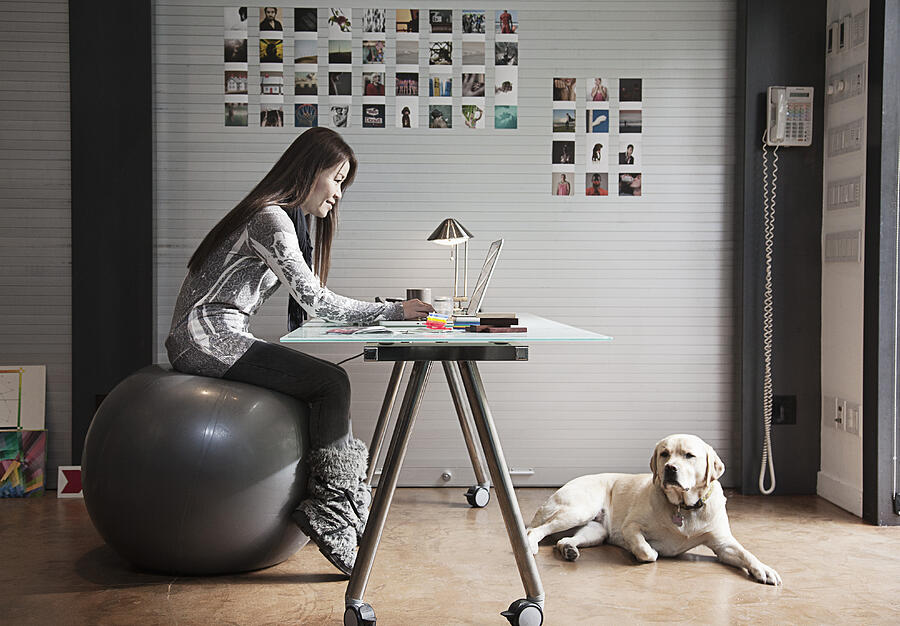 Japanese businesswoman sitting on exercise ball and working at desk Photograph by Hill Street Studios