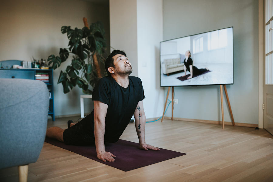 Japanese man taking online yoga lessons during lockdown in isolation Photograph by Visualspace