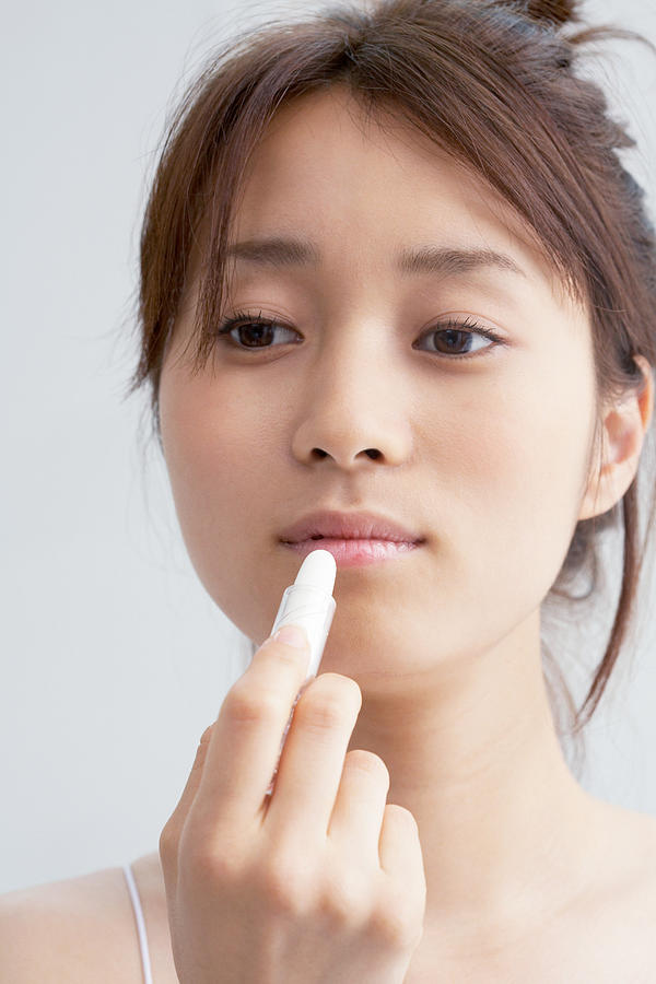 Japanese woman applying lipstick Photograph by Image Source
