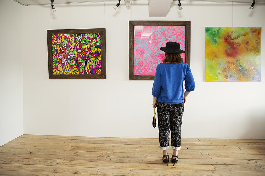 Japanese woman wearing hat standing in front of abstract painting in an art gallery. Photograph by Mint Images RF