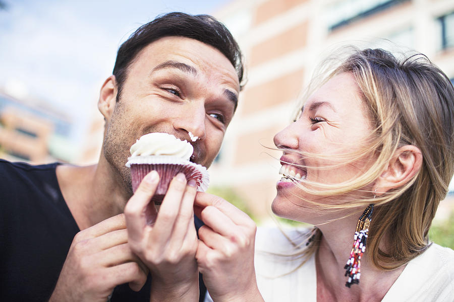 Joyful couple eating cupcake outdoors Photograph by DrGrounds