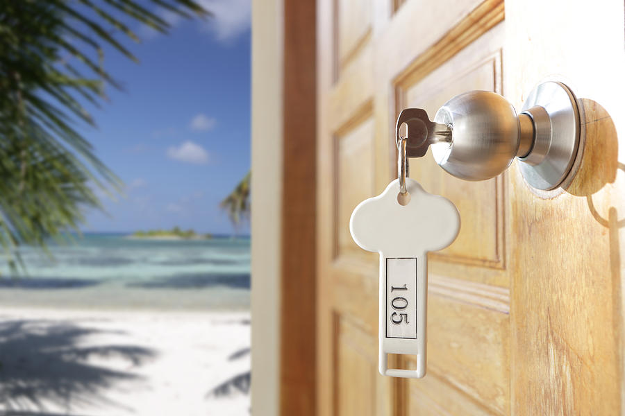 Key in open hotel door, beach in background Photograph by Peter Cade