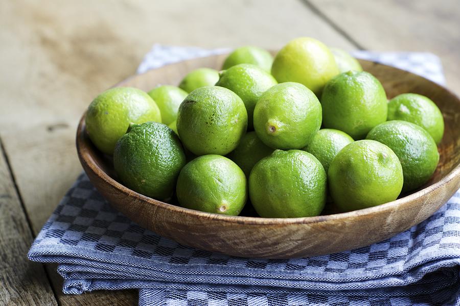 Key limes, Citrus aurantiifolia, in a wooden bowl Photograph by Westend61