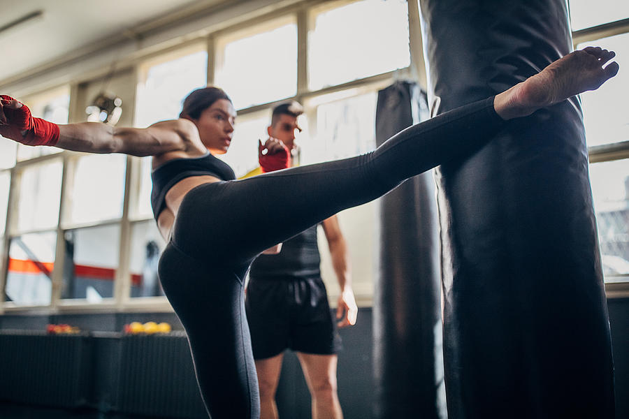Kick box instructor looking how woman kick boxer is kicking punching bag on kick box class Photograph by South_agency