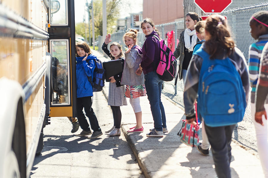 Kids in line waiting to get on school bus saying goodbye. Photograph by Martinedoucet