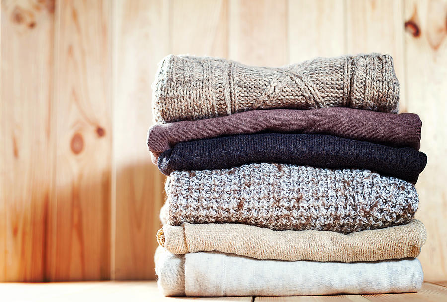 Knit cozy sweater folded in a pile on wooden background .Warm the concept Photograph by Keira01