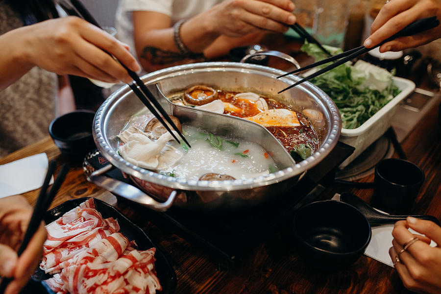Korean hot pot meal. Hands taking food with chopsticks. Photograph by Daviles