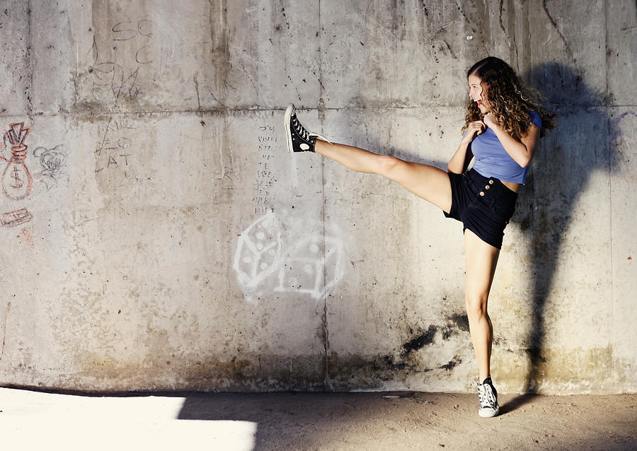 Kung-fu fighting? Curly-haired cutie high kicks energetically by stone wall Photograph by RapidEye