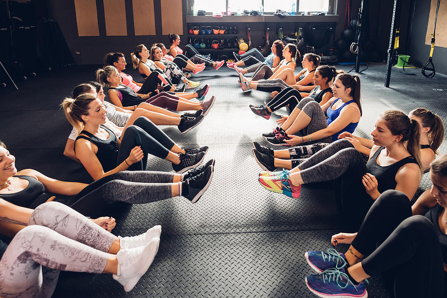 Large group of women training in gym, sitting in rows on floor with legs raised Photograph by Eugenio Marongiu