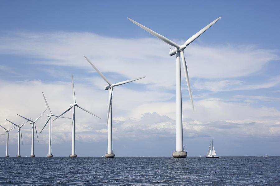 Large white windmills in the sea with a sailboat Photograph by Pareto