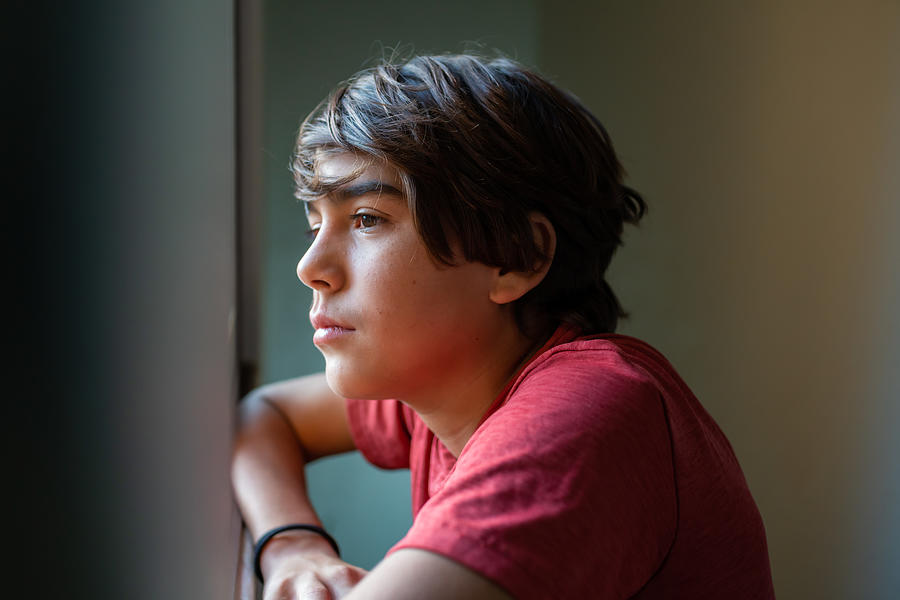 Latinx Preadolescent Boy Looking Out Through Window, Reflecting, Relaxing, Pensive. Photograph by MarsBars
