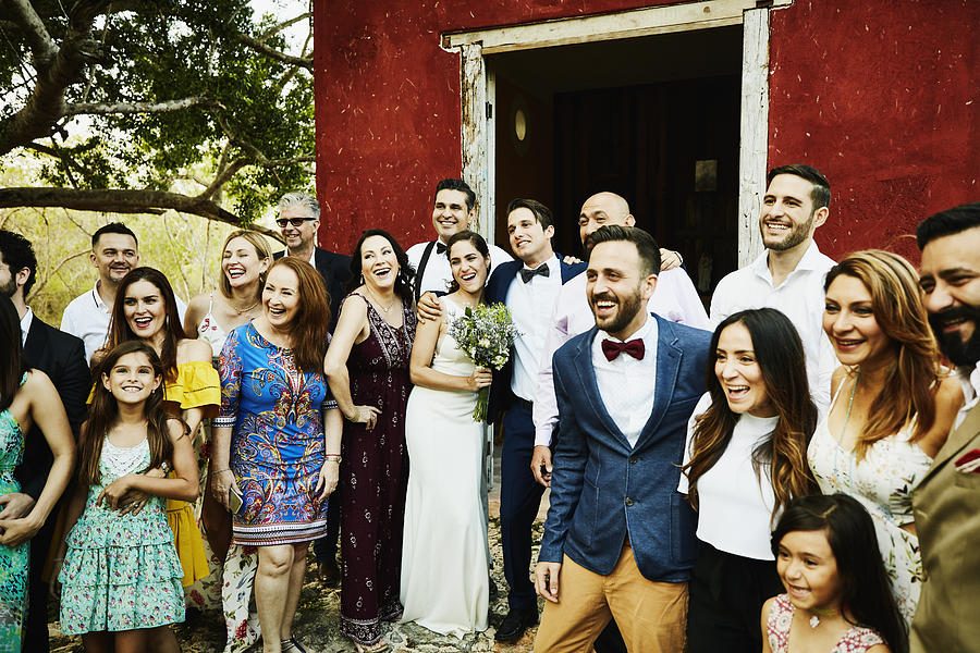 Laughing and smiling wedding party posing for group photo in front of chapel after wedding ceremony Photograph by Thomas Barwick