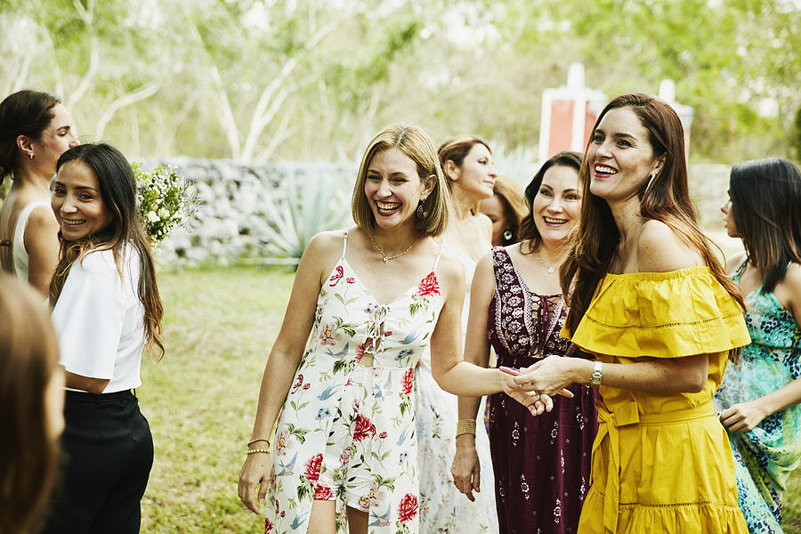 Laughing female friends in discussion during outdoor wedding reception Photograph by Thomas Barwick