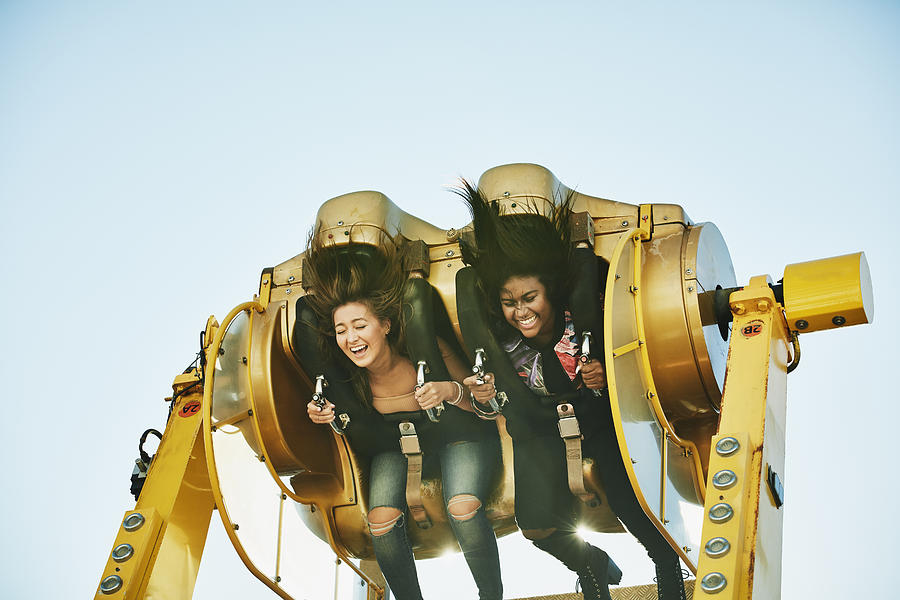 Laughing female friends spinning upside down on amusement park ride Photograph by Thomas Barwick