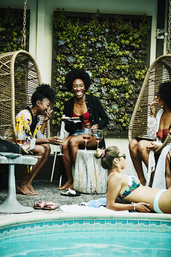 Laughing friends sharing food and drink during party at hotel pool Photograph by Thomas Barwick