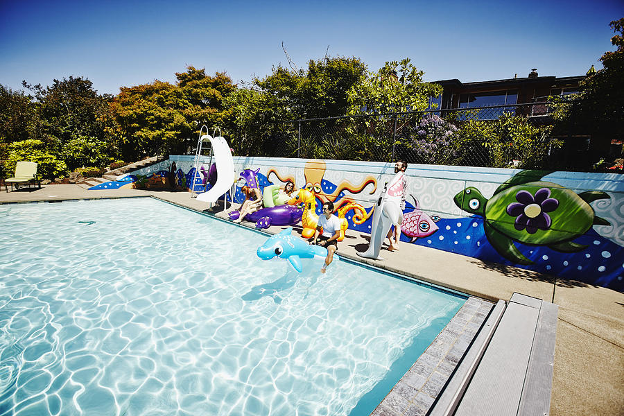 Laughing friends sitting pool side Photograph by Thomas Barwick