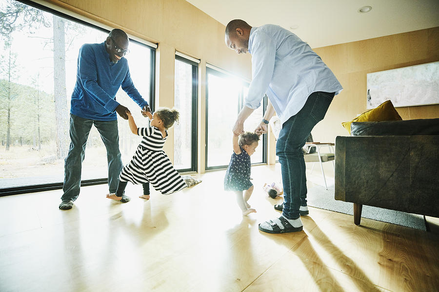 Laughing grandfather and father dancing with granddaughter and daughter in living room Photograph by Thomas Barwick