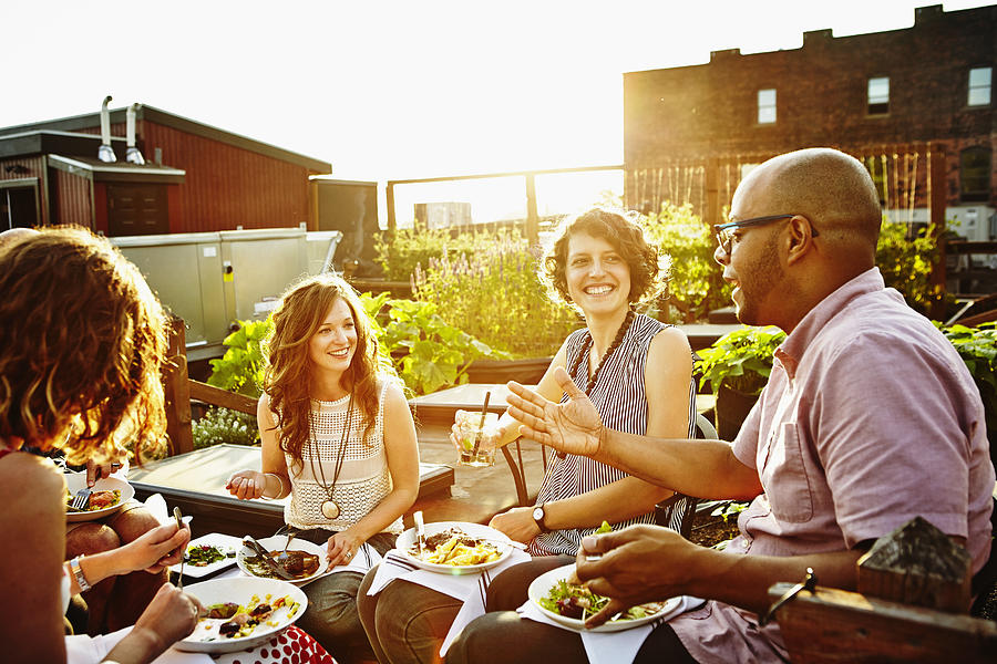 Laughing group of friends dining in rooftop garden Photograph by Thomas Barwick