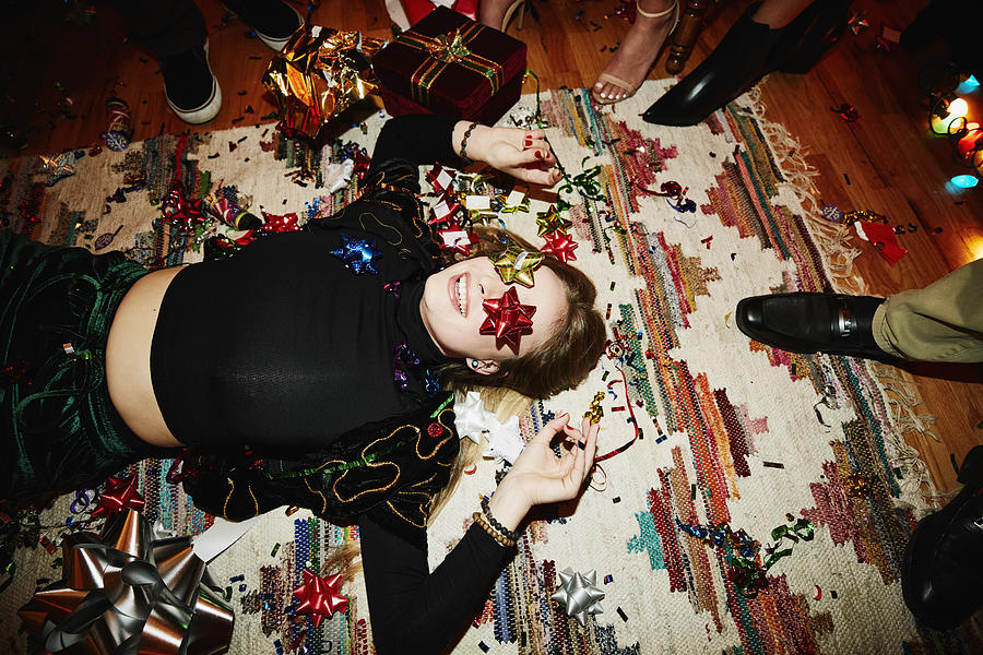Laughing woman lying on floor with bows over eyes during holiday party with friends Photograph by Thomas Barwick