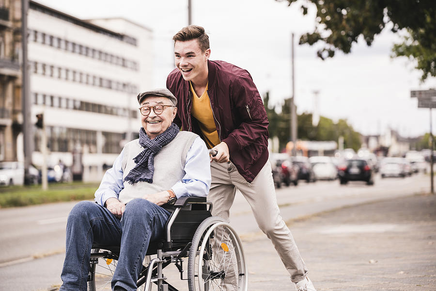 Laughing young man pushing happy senior man in wheelchair Photograph by Westend61