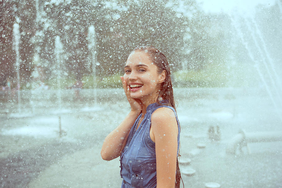 Laughing young woman in wet clothes standing in water splashes of fountain Photograph by Nina Sinitskaya