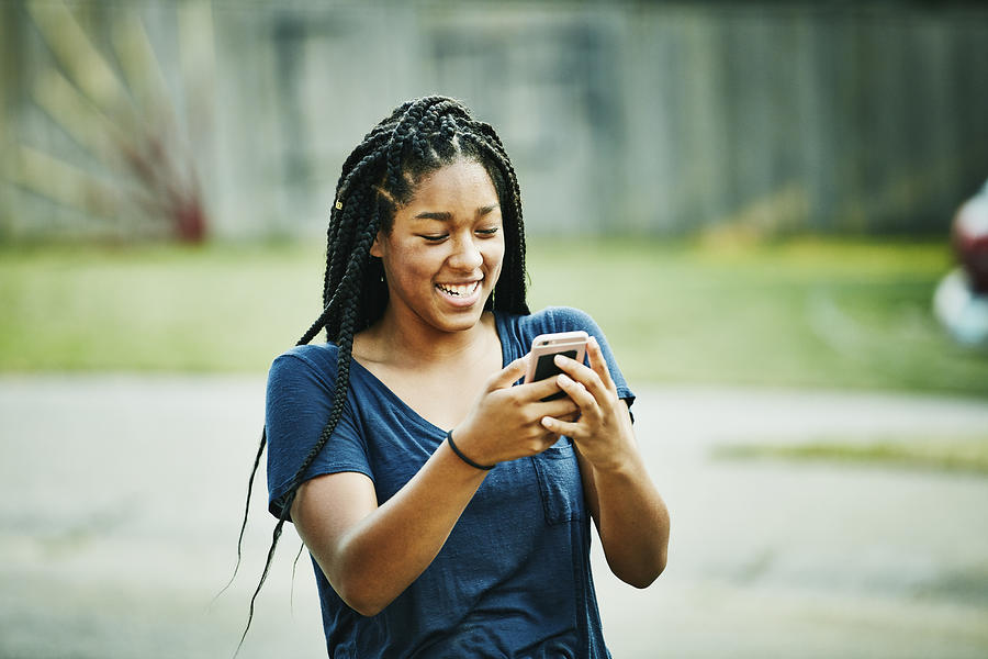 Laughing young woman looking at smartphone on summer evening Photograph by Thomas Barwick