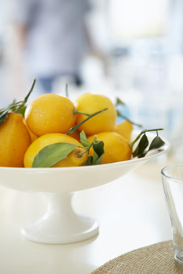 Lemons in bowl on table, person standing in backgroundclose-up Photograph by Maren Caruso