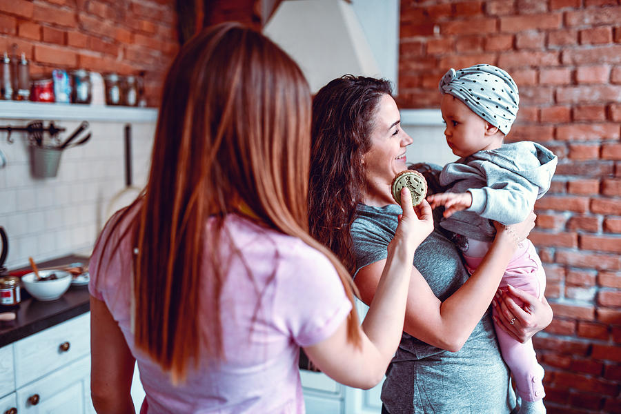 Lesbian Couple Giving Cookie To Their Baby Daughter Photograph by AleksandarGeorgiev