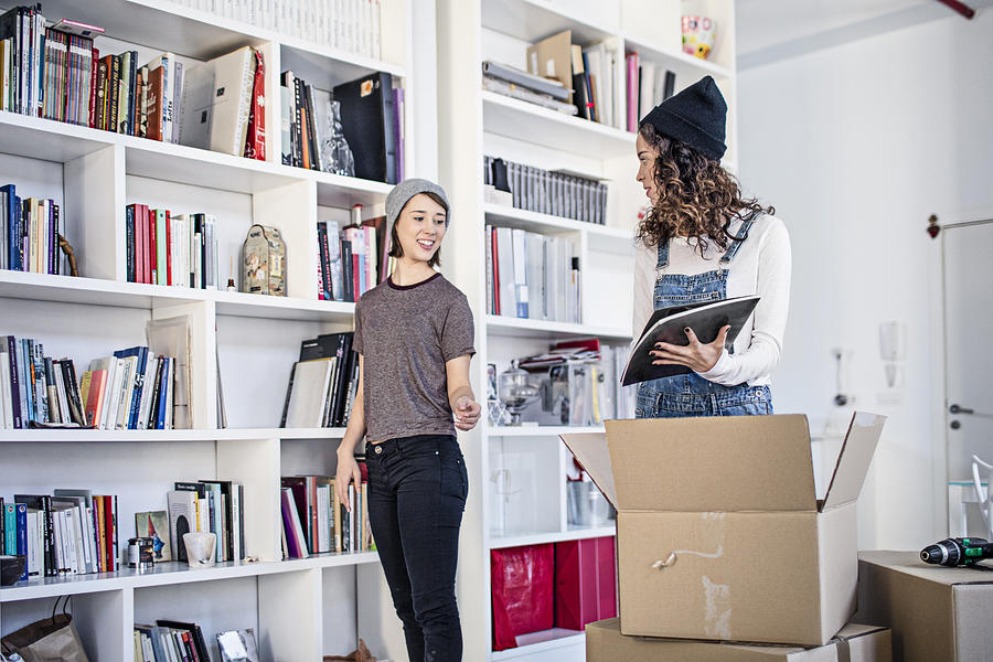 Lesbian couple unpacking cardboard box in living room Photograph by Xavier Arnau