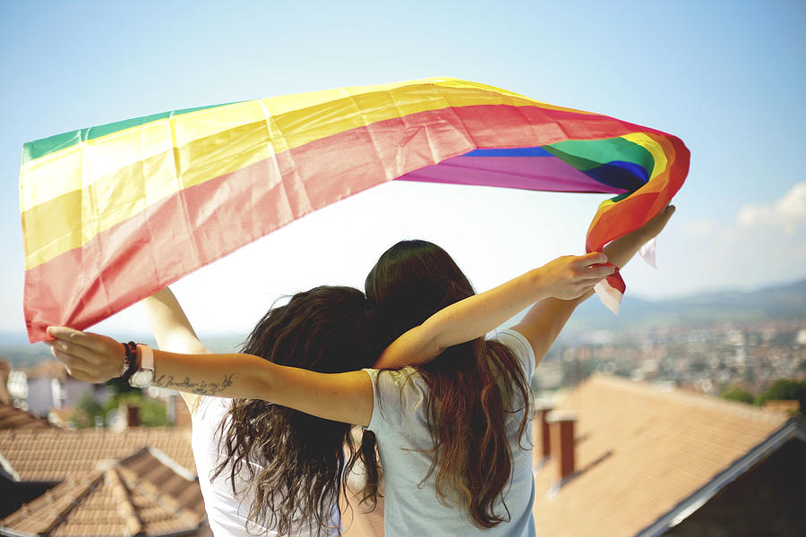 LGBT Lesbian couple moments happiness concept. Holding rainbow flag outdoors Photograph by MarijaRadovic