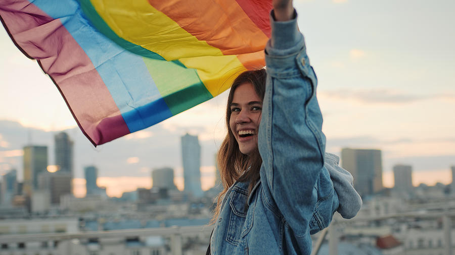 LGBT proud. Happy woman holding lgbt flag. Rooftop view Photograph by Janiecbros