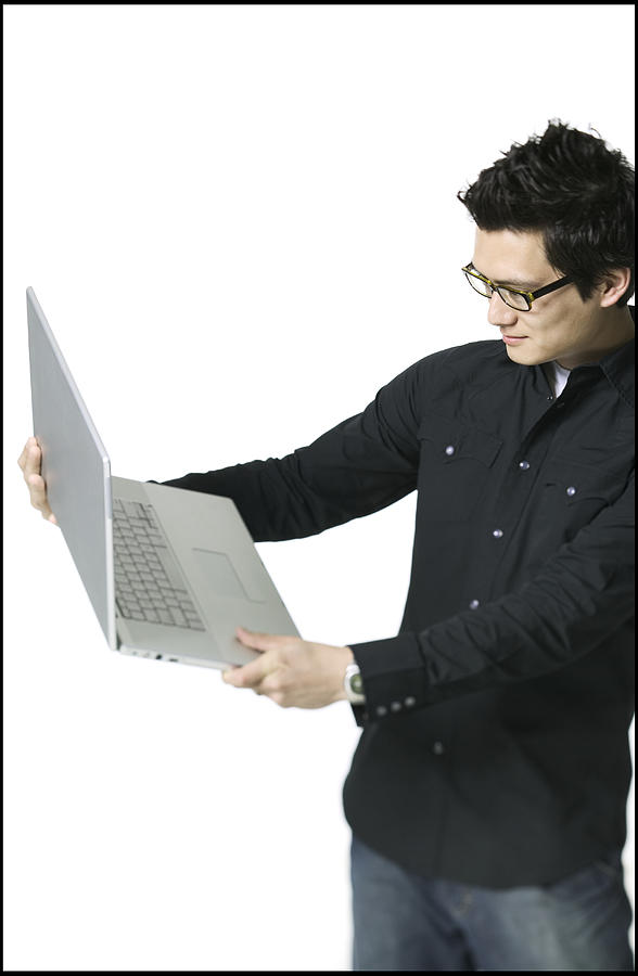 Lifestyle Portrait Of A Young Adult Male In A Black Shirt As He Holds Out And Examines His Laptop Computer Photograph by Photodisc