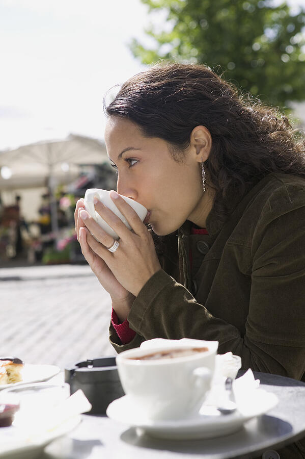 Lifestyle Portrait Of A Young Adult Woman As She Sips From Her Cup At An Outdoor Cafe Photograph by Photodisc