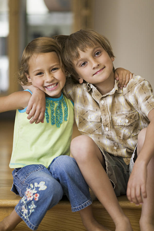 Lifestyle Portrait Of Two Sibling Children As They Put Their Arms Around Each Other And Smile Photograph by Photodisc