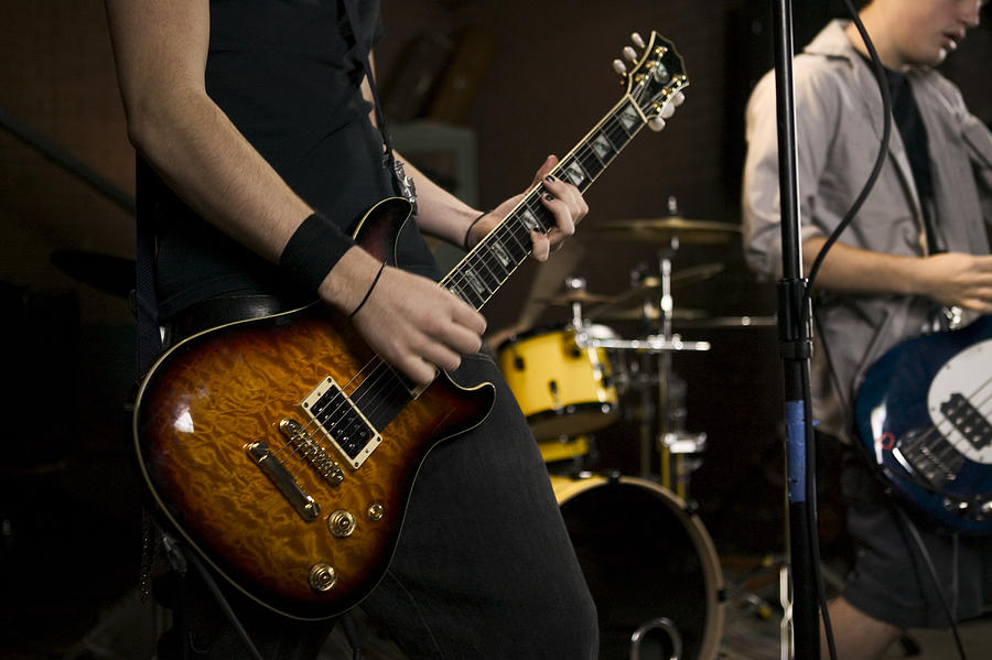 Lifestyle Portrait Of Two Teenage Males As They Wildly Practice Their Guitars With A Band Photograph by Photodisc