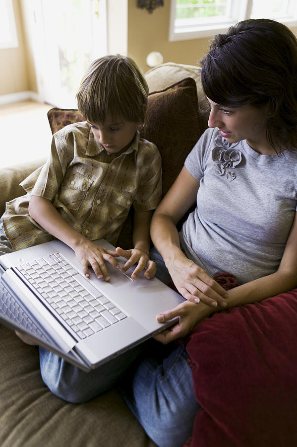Lifestyle Shot Of A Mother Sitting On A Couch With Her Son As They Use A Computer Photograph by Photodisc