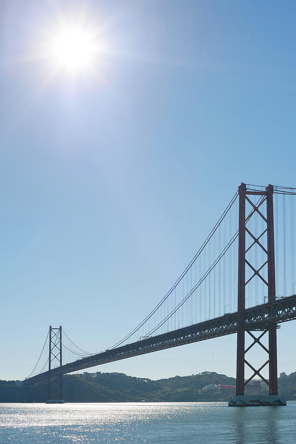Lisbon 25 april suspension bridge againt blue sky and sun Photograph by Philippe Lejeanvre