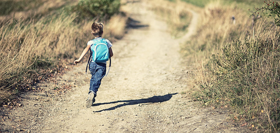 Little boy wearing backpack running on a dirt road Photograph by Imgorthand