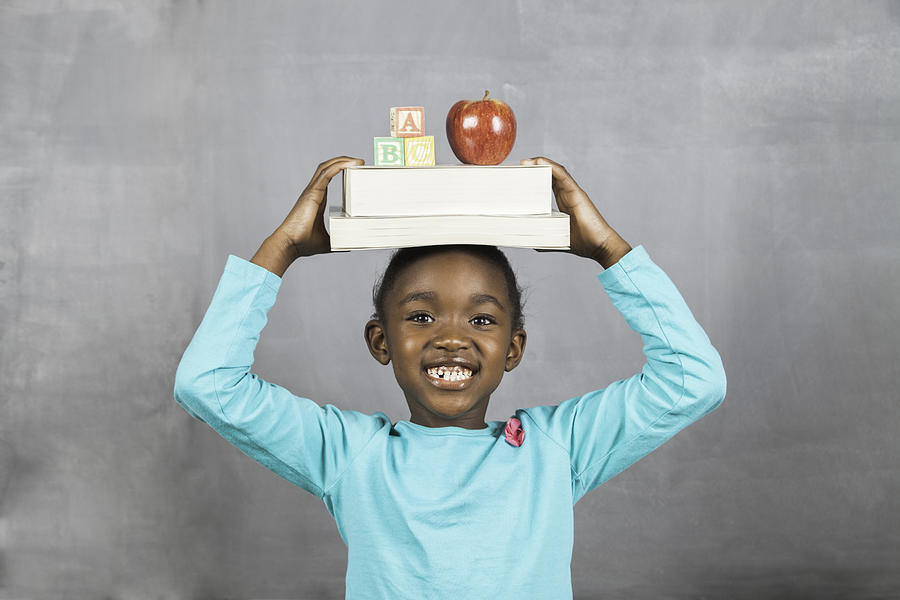 Little girl balancing books and an apple on her head Photograph by AfricaImages