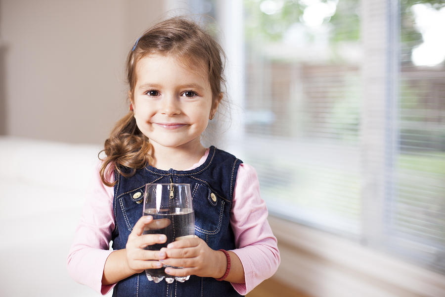 Little girl holding a water glass, looking at the camera Photograph by Vitapix