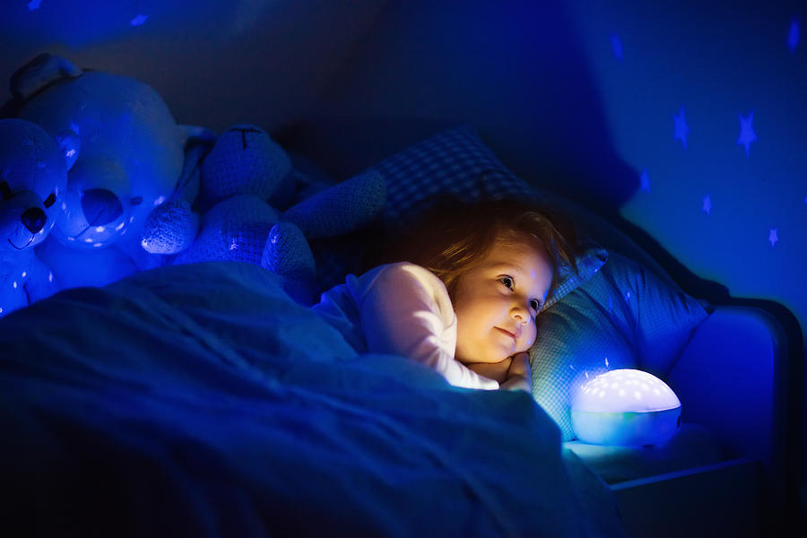 Little girl in bed with night lamp in dark nursery Photograph by FamVeld