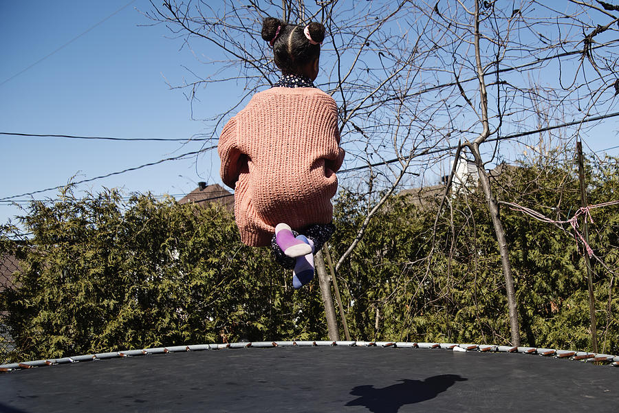 Little girl jumping on trampoline outdoors in springtime. Photograph by Martinedoucet