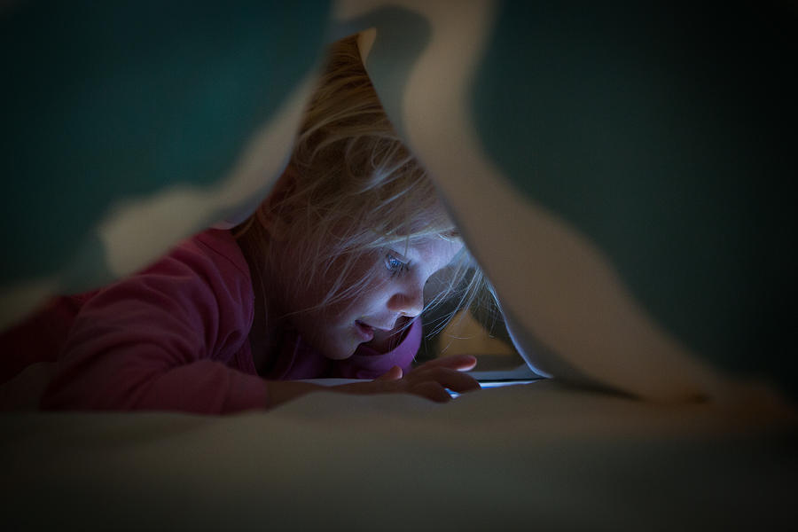 Little girl on cell phone under duvet Photograph by Nattrass