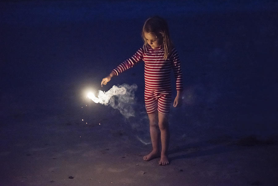 Little girl playing with bengal fire on the beach at dusk. Photograph by Martinedoucet