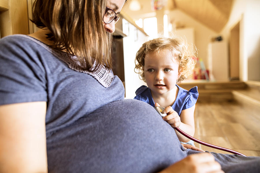 Little girl with stethoscope on belly of her pregnant mother. Photograph by Halfpoint Images