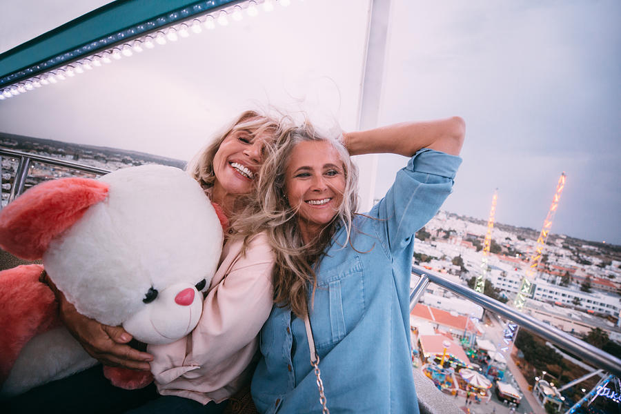 Loving mature friends laughing on amusement park ferris wheel ride Photograph by Wundervisuals