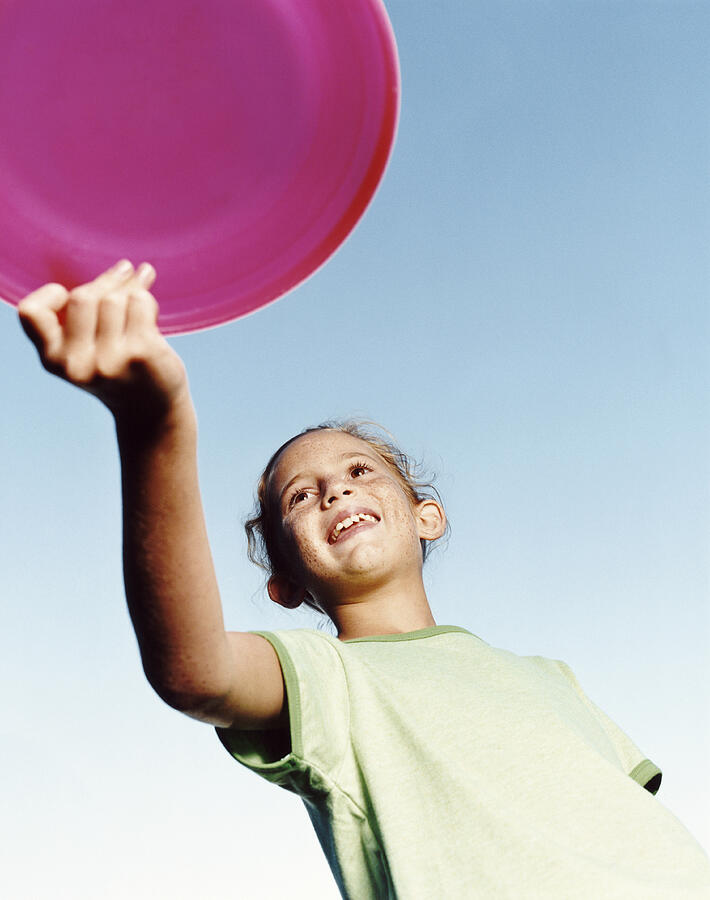 Low Angle of a Young Girl Holding a Pink Frisbee Photograph by Digital Vision.
