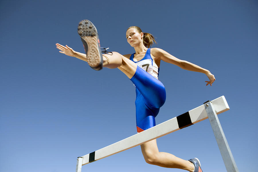 Low Angle Shot of a Determined Female Athlete Jumping Over a Hurdle Photograph by John Cumming