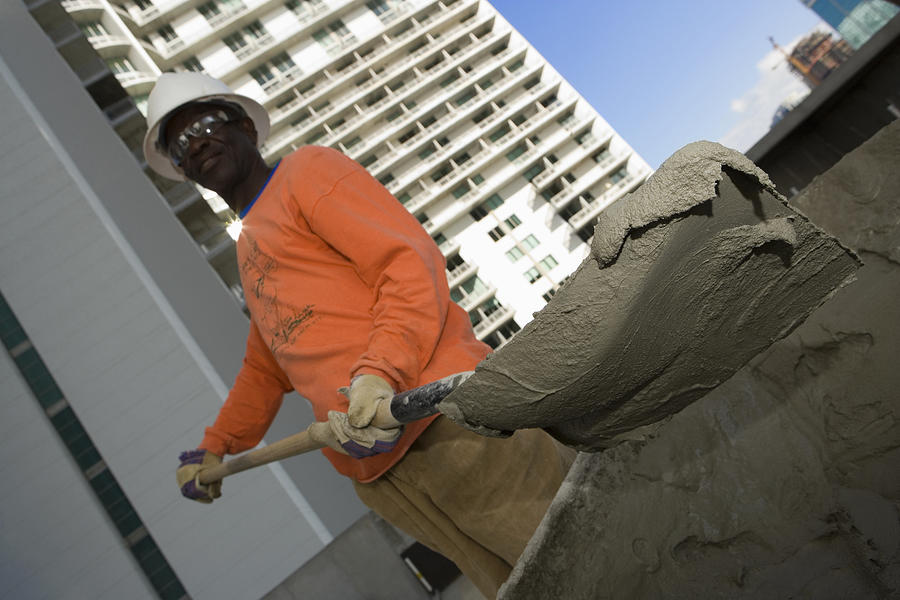Low angle view of a male construction worker shoveling cement Photograph by Glowimages