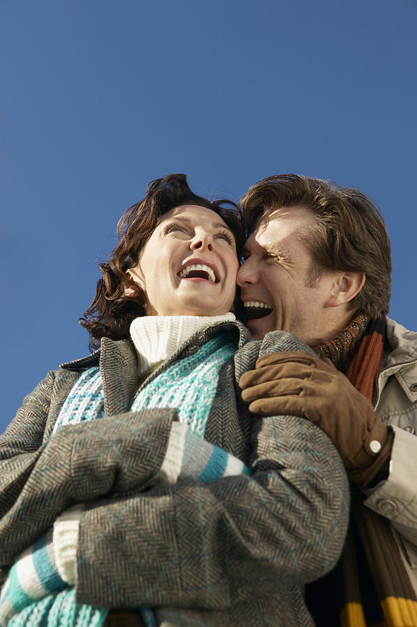 Low Angle View of a Mature Couple in Winter Clothing Embracing and Laughing Photograph by Digital Vision.